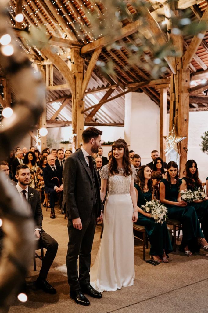 Bride and groom holding hands at wedding ceremony inside Pangdean Barn 