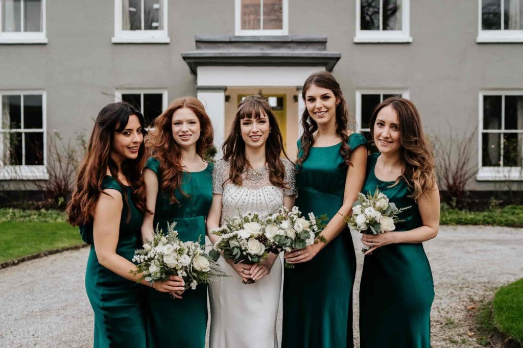 Bride & bridesmaids with emerald green dresses holding bouquets of white flowers at Pangdean Barn