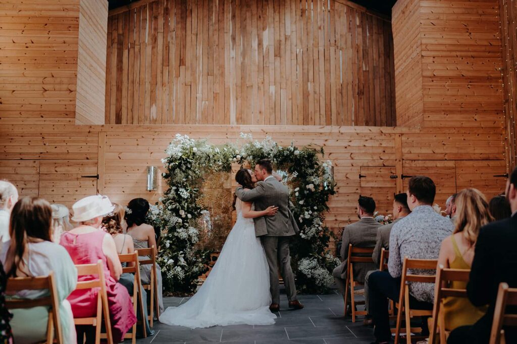 bride and groom kissing under floral arch at chafford park estate in Kent